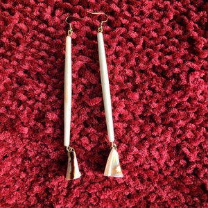 May include: A pair of long, white, shell earrings with gold hooks. The earrings are made from natural materials and have a unique, organic look.
