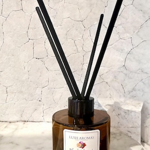 May include: A brown glass reed diffuser with black reeds. The label reads "Lush Aromas Black Plum & Rhubarb". The diffuser is 100ml. The background is a white, cracked-stone pattern.