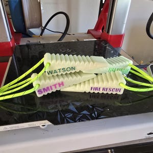 May include: Three white plastic fire rescue wedges with green and purple text. The wedges are connected by a bright yellow rope. The text on the wedges reads "FIRE RESCUE", "SMITH", and "WATSON".