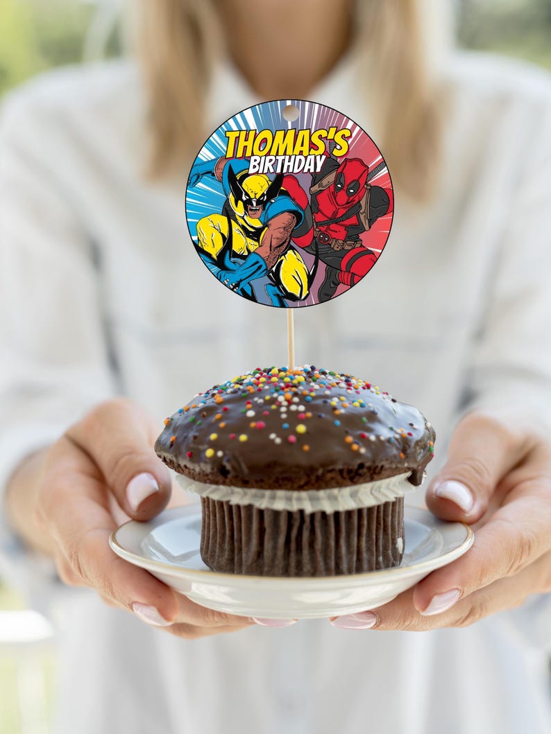 May include: A round cake topper with a picture of Wolverine and Deadpool. The topper says "Thomas's Birthday".