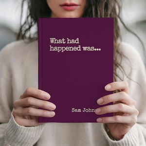 May include: A hardcover book with a deep purple cover. The title "What had happened was..." is printed in white, along with the author's name, Sam John. The book is held in front of a person.