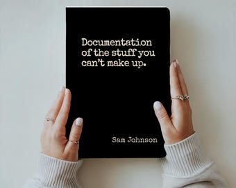May include: A black notebook with the text "Documentation of the stuff you can't make up" and the name "Sam Johnson" in white. The notebook is held by two hands with rings.