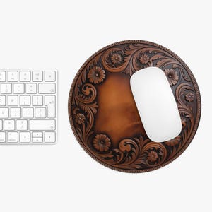 May include: Round brown leather mousepad with a floral carved design and a white computer mouse. The mousepad has a decorative border and a lighter brown center. A white keyboard is visible in the background.