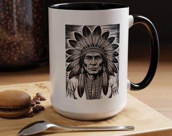 Może przedstawiać: Biały ceramiczny kubek z czarnym uchwytem i obramowaniem. Kubek przedstawia czarno-białą ilustrację indiańskiego wodza w pióropuszu. Kubek stoi na drewnianej powierzchni z łyżką i ciastkiem.