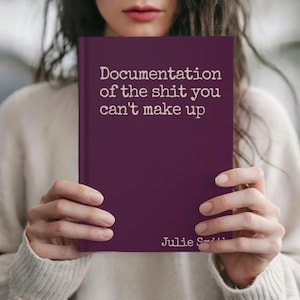 May include: A person holds a book with a deep purple cover. The book's title, in white text, reads "Documentation of the shit you can't make up". The author's name, Julie Smith, is printed at the bottom of the cover.