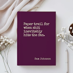May include: A deep purple hardcover journal with the quote "Paper trail for when shit inevitably hits the fan" and the author's name, Sam Johnson. The journal is on a white surface with a pen, a cup of coffee, and small white flowers.