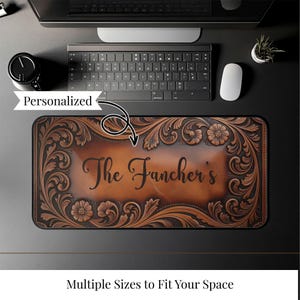 May include: A personalized brown leather desk mat with floral and scrollwork designs. The mat features the name "The Fancher's" in elegant script. The mat is rectangular and designed to fit under a keyboard and mouse.