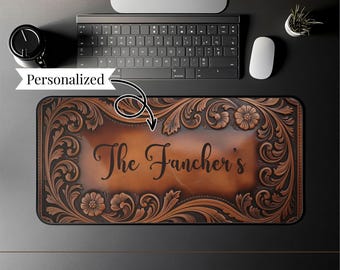 May include: A personalised brown leather desk mat with floral and scrollwork designs. The mat features the name "The Fancher's" in elegant script. The mat is rectangular and designed to fit under a keyboard and mouse.