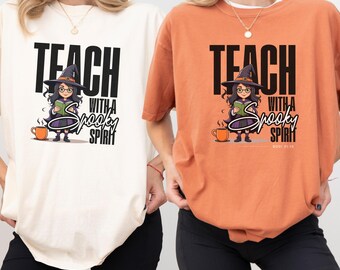 May include: Two t-shirts, one cream and one orange, each featuring a graphic of a witch wearing glasses and a hat, holding a book. The text reads "TEACH WITH A SPOOKY SPIRIT" in black and white lettering, accompanied by an orange mug illustration.