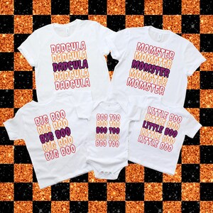 Puede incluir: Camisetas blancas con texto de Halloween en naranja, morado y rojo. Las camisetas dicen "DADCULA", "MOMSTER", "BIG BOO", "BOO TOO" y "LITTLE BOO". Las camisetas est&aacute;n dispuestas sobre un fondo a cuadros negro y naranja.