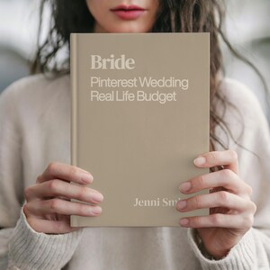 May include: A beige book titled "Bride" with the text "Pinterest Wedding Real Life Budget" in white. The author's name, Jenni Smith, is printed at the bottom. The book is held in front of a person.