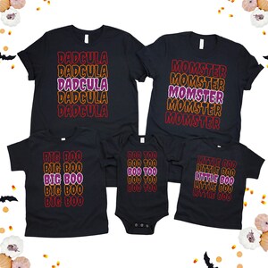 Puede incluir: Un conjunto de camisetas negras y un body con tem&aacute;tica de Halloween. Las camisetas presentan las frases "DADCULA", "MOMSTER", "BIG BOO", "BOO TOO" y "LITTLE BOO" en un dise&ntilde;o apilado con letras naranjas, moradas y rojas.