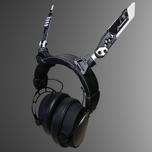 May include: Black headphones with a unique design featuring two black and white arms extending from the top of the headband. The arms are attached to the headband with a black and white clip.