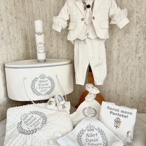 Pode incluir: Um conjunto de roupa de batismo branco, incluindo fato, chapéu, sapatos, cobertor e acessórios. O conjunto apresenta detalhes bordados e o nome "Albert Daniel" com a data "1 Februarie 2025".