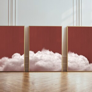 Op de afbeelding: Drie ingelijste prints met een rode achtergrond en een witte wolk onderaan elke print.