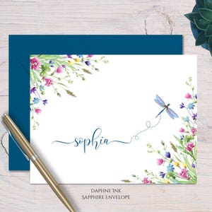 May include: A white card with a blue dragonfly and watercolor flowers in the corner. The card has the name "sophia" written in cursive on it. The card is on a blue envelope with the text "Daphne Ink Sapphire Envelope" at the bottom.