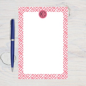 May include: A pink and white notepad with a geometric pattern border. The notepad has a circle in the top right corner with the initials "ACC" in black.