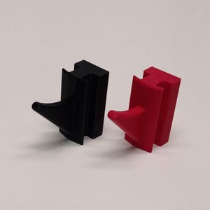 May include: Two 3D-printed objects. One is black, the other is red. Each has a rectangular base with a curved, conical projection extending from one side. The objects are designed to fit together.