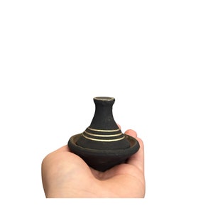Puede incluir: Un pequeño tagine negro con ribetes dorados, sostenido en una mano.