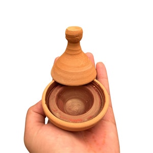Puede incluir: Una pequeña tagine de terracota con tapa, abierta y lista para cocinar. La tagine es una olla de cocción tradicional marroquí.