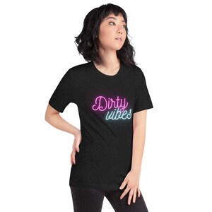 Puede incluir: Una camiseta negra con el texto "Dirty vibes" en letras de neón rosa y azul.