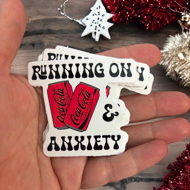 May include: White sticker with black text that reads "Running on Y & Anxiety" with a retro font. Two red Coca-Cola cans are featured on the sticker, one with "Zero Sugar" printed on it.