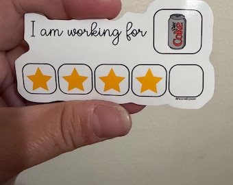 May include: A white rectangular sticker with rounded edges featuring the black text 'I am working for' next to an illustration of a silver Diet Coke can. Below the text are five square outlines, four of which contain solid yellow stars.