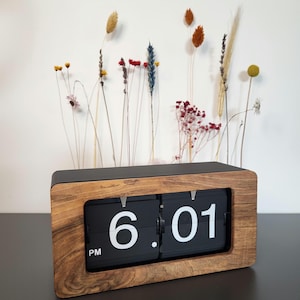 Könnte beinhalten: Eine Holz-Flip-Uhr mit schwarzen Zahlen, die 18:01 Uhr anzeigen. Die Uhr hat einen dunklen Holzrahmen und einen schwarzen Hintergrund.