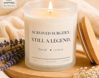 May include: A frosted glass candle with a lit wick and a wooden lid. The label reads: SURVIVED SURGERY. STILL A LEGEND. David 12/08/26. It includes the text 8OZ SOY and STARRY GEM STUDIO. The candle is placed on a round wooden base.