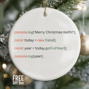 May include: A white, round Christmas ornament with gold string, featuring code that says "Merry Christmas Keith!" and the current year. The ornament is set against a blurred background of a Christmas tree with ornaments.