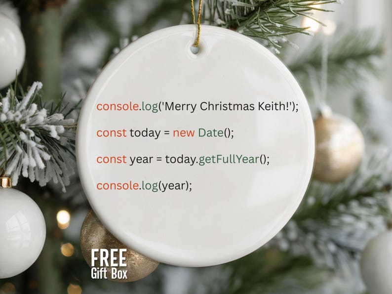 May include: A white, round Christmas ornament with gold string, featuring code that says "Merry Christmas Keith!" and the current year. The ornament is set against a blurred background of a Christmas tree with ornaments.