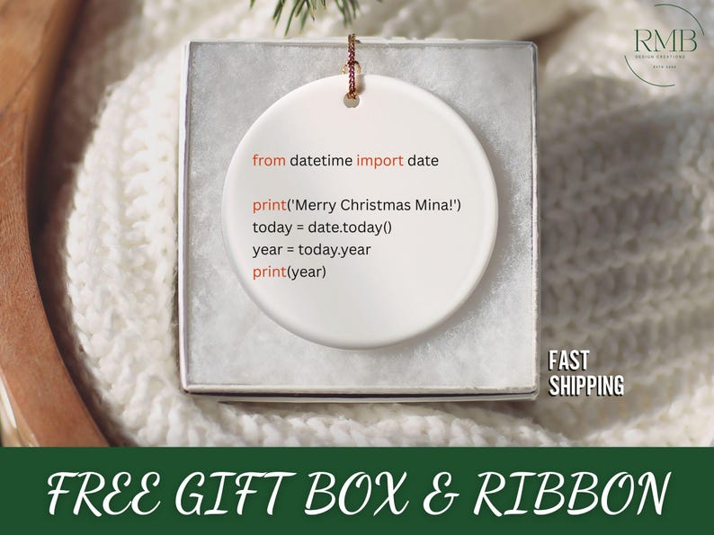 May include: A white ceramic Christmas ornament with a Python code snippet printed on it. The code includes a greeting and the current year. The ornament is in a gift box with a ribbon.