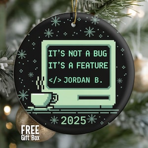 May include: Black and green Christmas ornament with a retro computer design. The text reads "IT'S NOT A BUG IT'S A FEATURE" and "2025". Includes a coffee cup graphic and the name "JORDAN B."