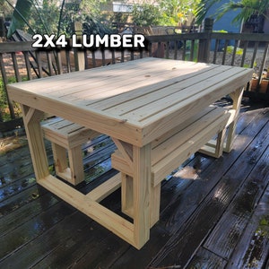 K&ouml;nnte beinhalten: Ein h&ouml;lzerner Picknicktisch mit zwei B&auml;nken, hergestellt aus 2x4 Holz. Tisch und B&auml;nke sind unbehandelt und haben eine nat&uuml;rliche Holzfarbe. Der Tisch steht auf einem Holzdeck.