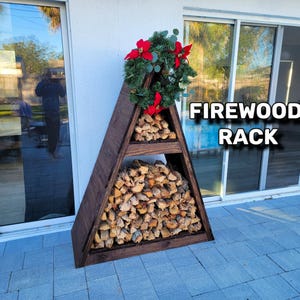Puede incluir: Un estante de leña de madera triangular con tres estantes, lleno de troncos de leña apilados. El estante está colocado afuera en un patio con una corona de flores de poinsettia rojas y hojas verdes en la parte superior. El texto "FIREWOOD RACK" es visible en la imagen.