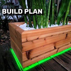 May include: A wooden planter box with a green light strip around the bottom. The planter is filled with white rocks and a green plant. The text "BUILD PLAN" is visible in the top left corner of the image.