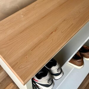 May include: A wooden shoe rack with a light brown top and white shelves. The rack is filled with various shoes, including sneakers and leather shoes. The top is made of wood and has a natural grain pattern.