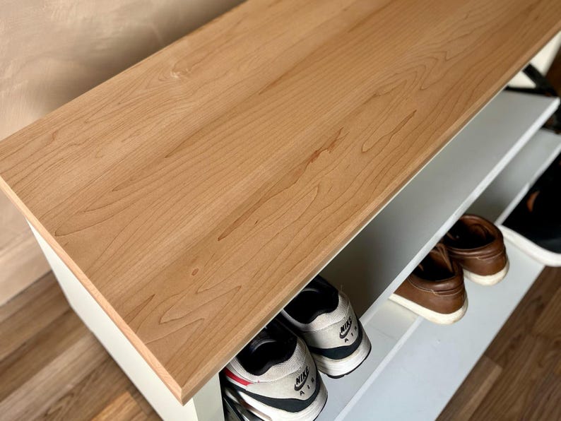May include: A wooden shoe rack with a light brown top and white shelves. The rack is filled with various shoes, including sneakers and leather shoes. The top is made of wood and has a natural grain pattern.