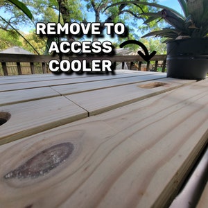 K&ouml;nnte beinhalten: Ein Holztisch mit einem Ausschnitt f&uuml;r eine K&uuml;hlbox. Der Text "REMOVE TO ACCESS COOLER" ist auf dem Tisch geschrieben.