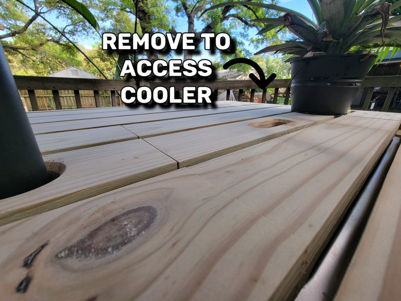 K&ouml;nnte beinhalten: Ein Holztisch mit einem Ausschnitt f&uuml;r eine K&uuml;hlbox. Der Text "REMOVE TO ACCESS COOLER" ist auf dem Tisch geschrieben.