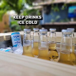 K&ouml;nnte beinhalten: Ein Holz-K&uuml;hlbox mit Eis und mehreren Flaschen eines hellgelben Getr&auml;nks. Die K&uuml;hlbox hat ein Schild mit der Aufschrift "KEEP DRINKS ICE COLD". Eine der Flaschen hat ein Etikett mit der Aufschrift "CO2 Coconut Water The Original".