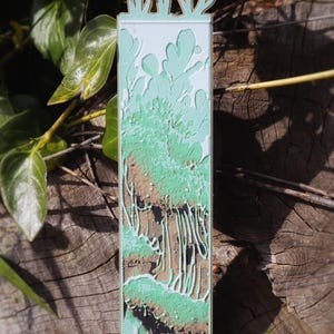 This bookmark is vibrant with green, depicting a mossy, organic landscape with dripping elements,  representing lush forest growth or nutrient-rich decomposition. Mushrooms appear to be growing from the top of the bookmark.