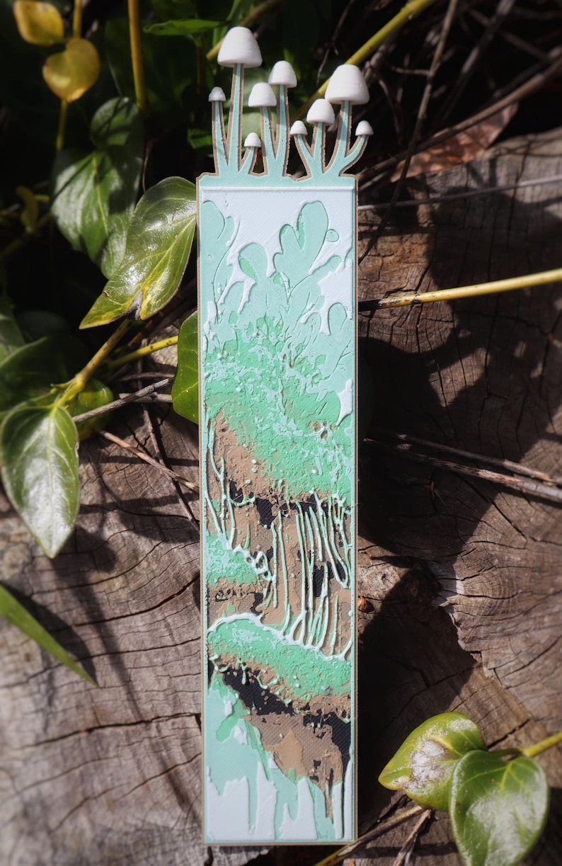 This bookmark is vibrant with green, depicting a mossy, organic landscape with dripping elements,  representing lush forest growth or nutrient-rich decomposition. Mushrooms appear to be growing from the top of the bookmark.