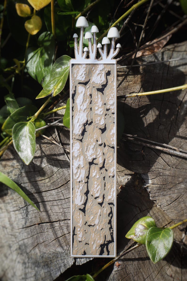 This bookmark displays a textured pattern resembling cracked tree bark, in shades of brown, beige, and black. Mushrooms appear to be growing from the top of the bookmark.