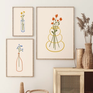 Puede incluir: Tres ilustraciones enmarcadas de flores en jarrones. La primera ilustraci&oacute;n presenta flores amarillas en un jarr&oacute;n azul. La segunda ilustraci&oacute;n presenta flores naranjas en un jarr&oacute;n dorado. La tercera ilustraci&oacute;n presenta flores azules en un jarr&oacute;n rojo.