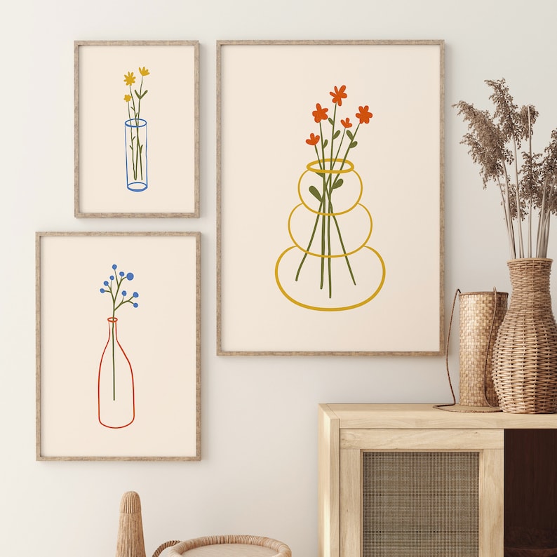 Puede incluir: Tres ilustraciones enmarcadas de flores en jarrones. La primera ilustraci&oacute;n presenta flores amarillas en un jarr&oacute;n azul. La segunda ilustraci&oacute;n presenta flores naranjas en un jarr&oacute;n dorado. La tercera ilustraci&oacute;n presenta flores azules en un jarr&oacute;n rojo.