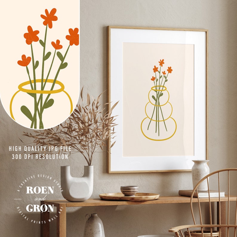 Puede incluir: Una impresi&oacute;n de arte digital de un ramo de flores naranjas en un jarr&oacute;n amarillo. El jarr&oacute;n est&aacute; hecho de tres c&iacute;rculos apilados. La impresi&oacute;n est&aacute; enmarcada y colgada en una pared sobre una mesa de madera.