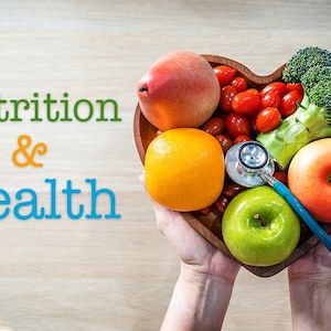 May include: A heart-shaped wooden bowl filled with fresh fruit and vegetables, including a pear, orange, apple, broccoli, and cherry tomatoes. A stethoscope is placed on top of the bowl, with the text "Nutrition & Health" visible in the background.