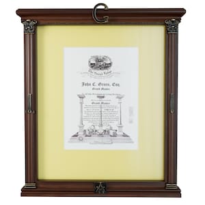 Peut inclure: Un document encadré dans un cadre en bois brun foncé. Le document contient du texte tel que "The Grand Lodge" et "John C. Green, Esq. Grand Master". Le cadre a des coins décoratifs et un "G" en métal en haut.