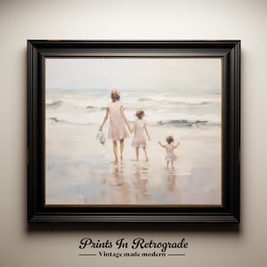 May include: A framed painting of three people walking on a beach. The people are wearing pink dresses and are walking away from the viewer. The beach is sandy and the water is blue. The painting is in a black frame.